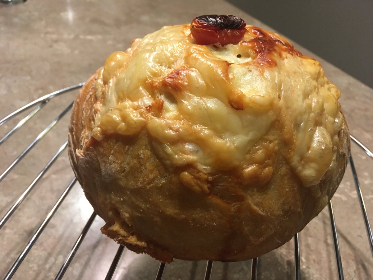 An extremely cheesy loaf of cheese bread with a blackened cherry tomato on top.