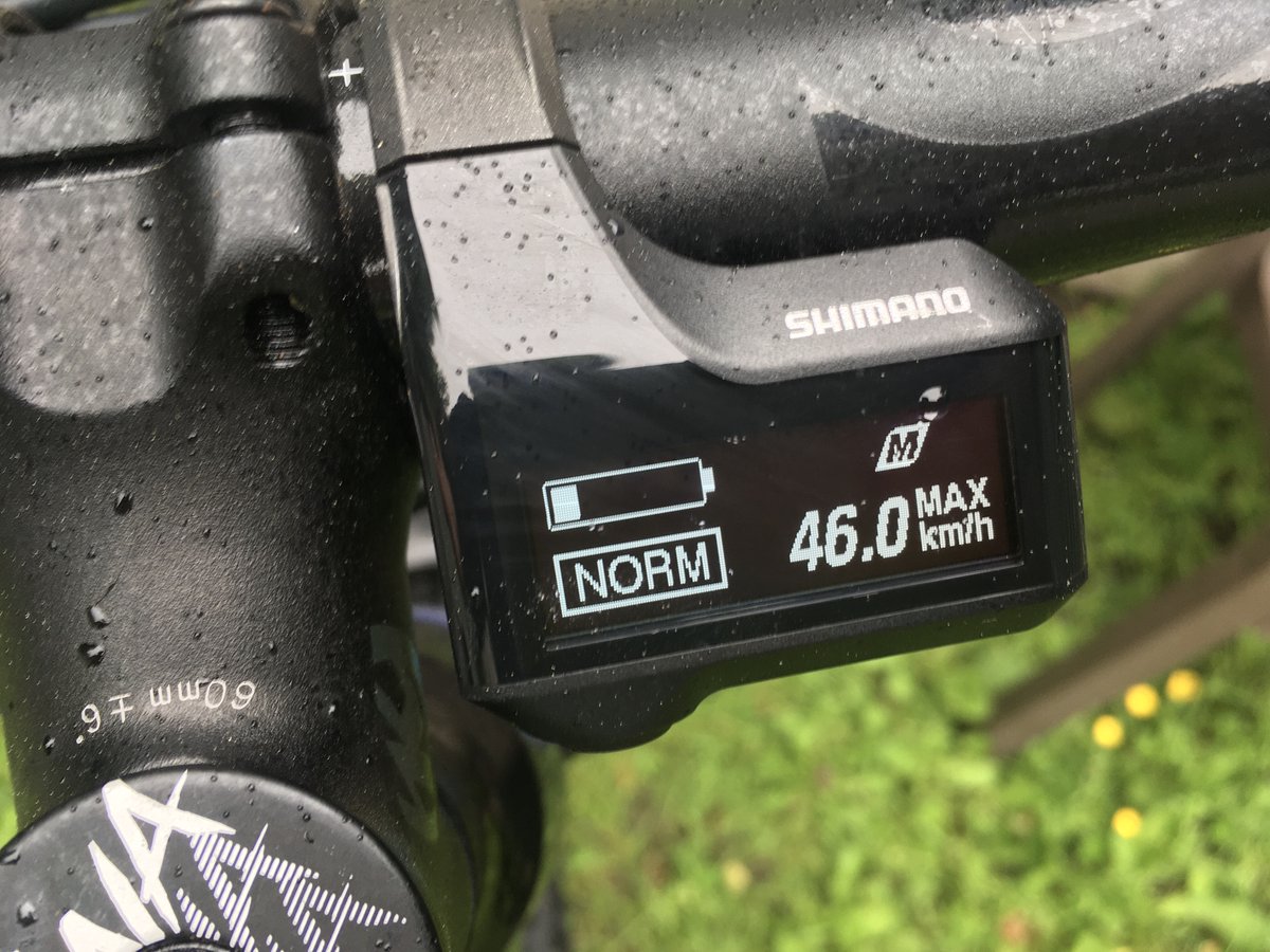 Bike handlebar with a screen showing speed and battery power. The battery is low, 1/5 bars, but the speed reads 46km/h. The bike is spattered with tiny droplets of rain.